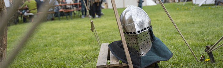 Ritterhelm liegt auf einem Holzkarren, der auf einer grünen Wiese steht.